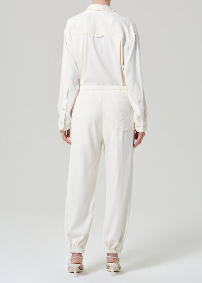 Person wearing a cream shirt and matching pants on a grey background