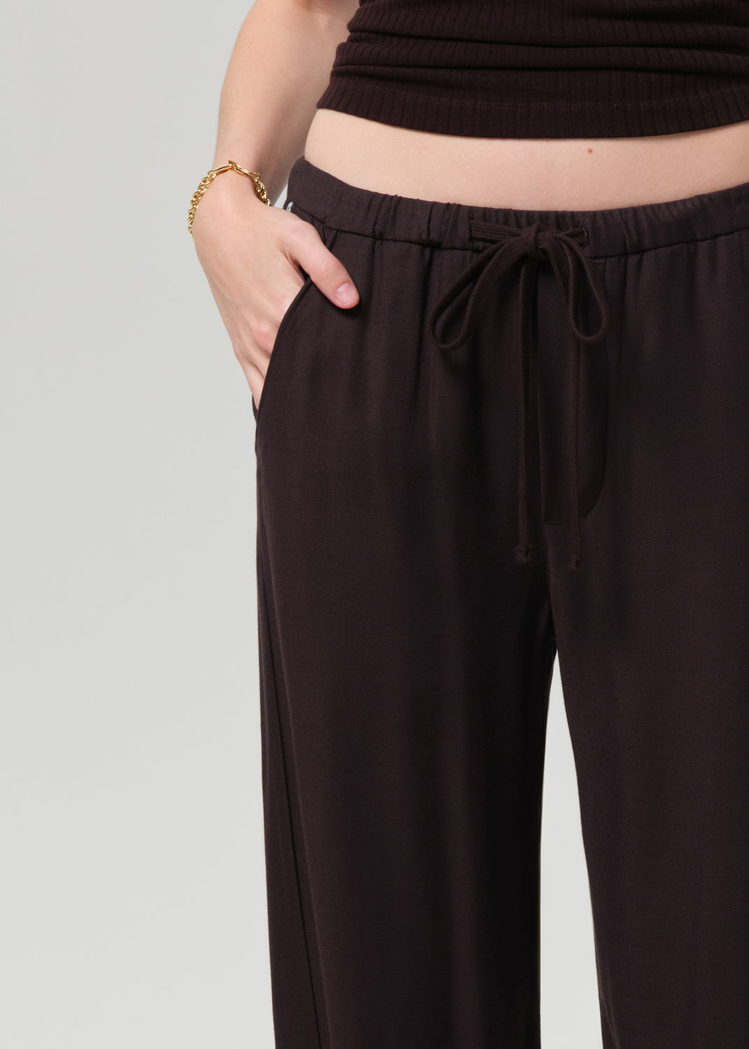 Person wearing a brown halter top and cuffed-ankle pants on a light gray background