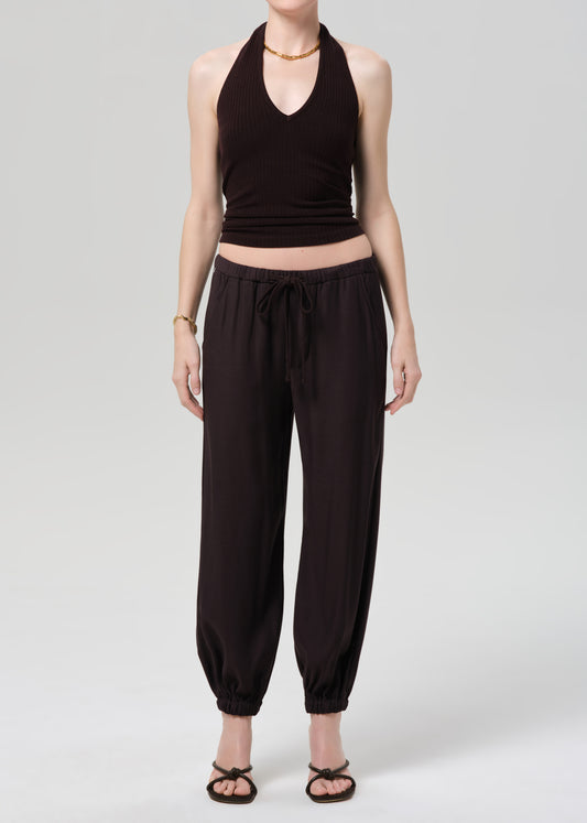 Person wearing a brown halter top and cuffed-ankle pants on a light gray background