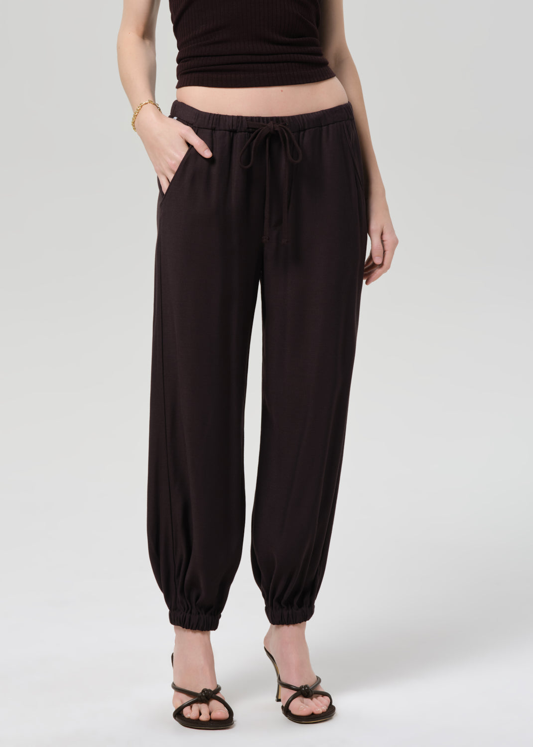 Person wearing a brown halter top and cuffed-ankle pants on a light gray background