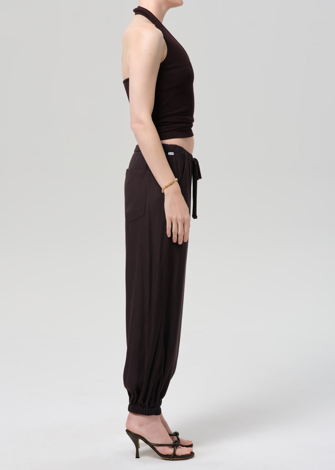 Person wearing a brown halter top and cuffed-ankle pants on a light gray background