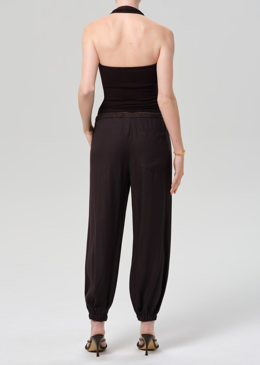 Person wearing a brown halter top and cuffed-ankle pants on a light gray background