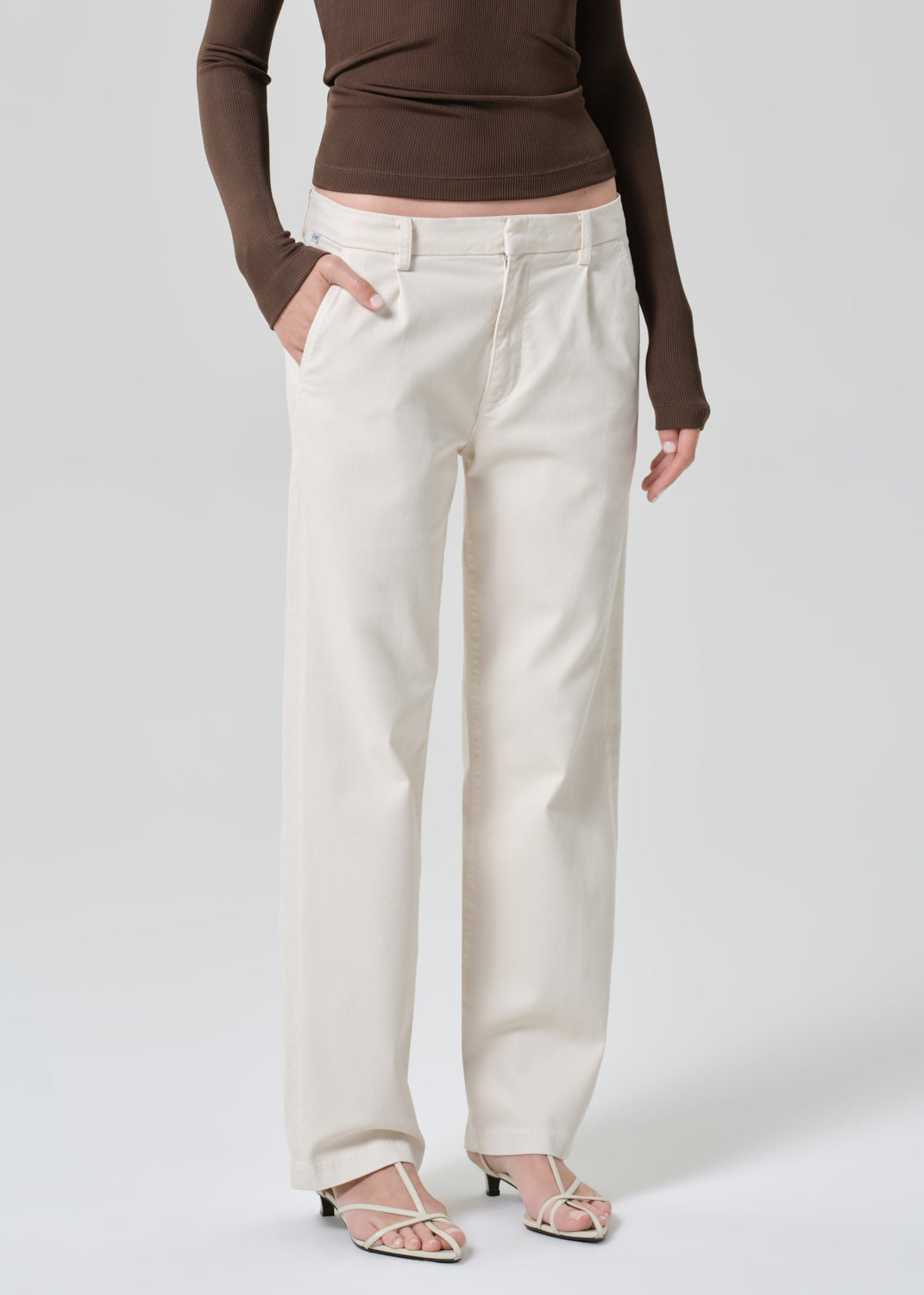 Person wearing a brown long-sleeve top and white pants on a plain background