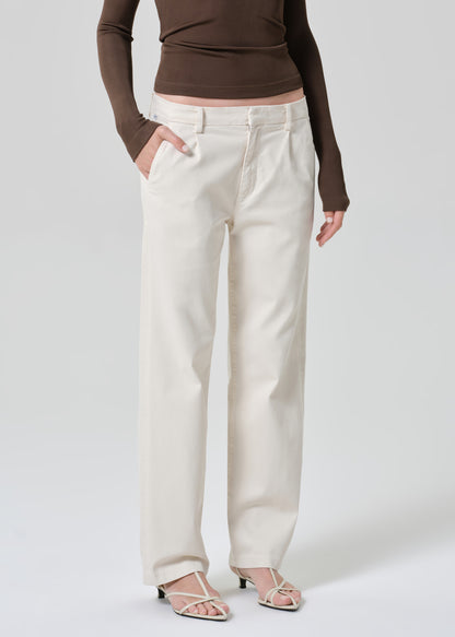 Person wearing a brown long-sleeve top and white pants on a plain background