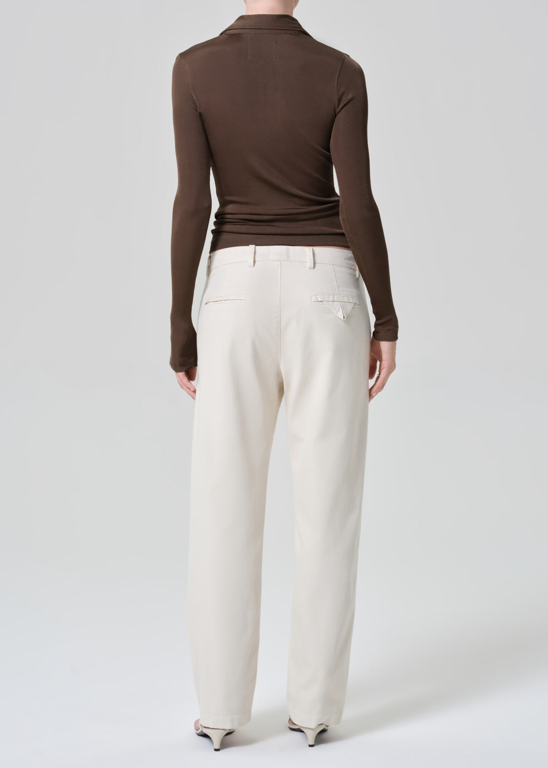 Person wearing a brown long-sleeve top and white pants on a white background