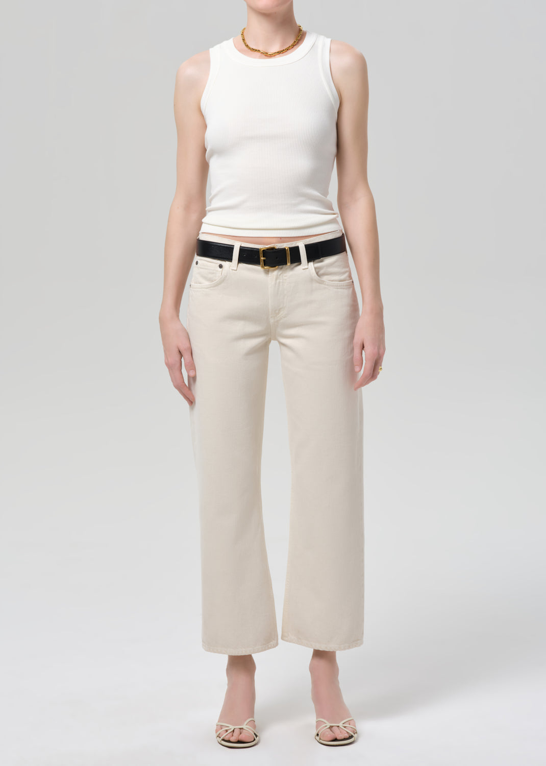 Person wearing a white sleeveless top and beige pants on a plain background