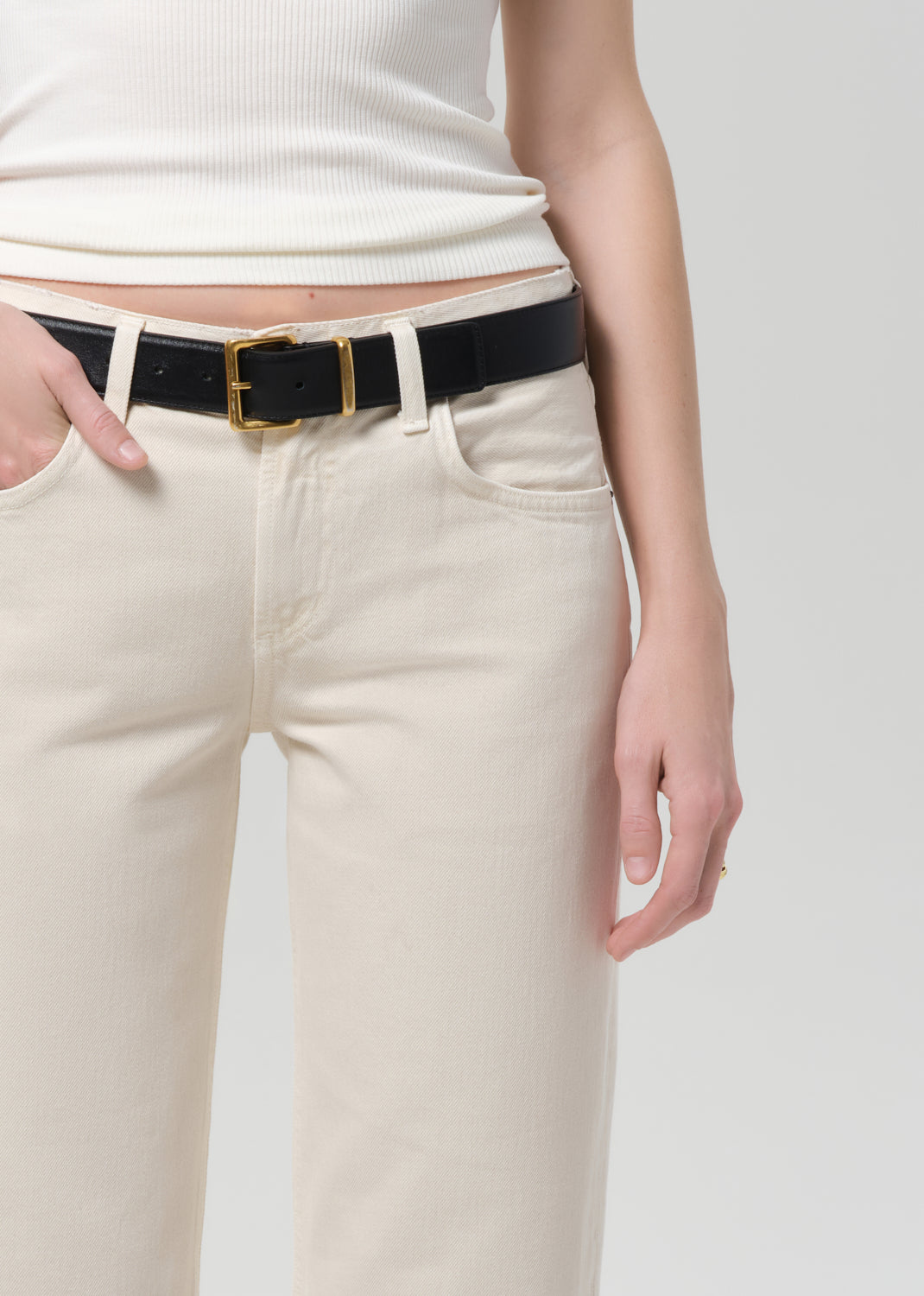 Person wearing a black belt with a gold buckle on beige jeans against a grey background