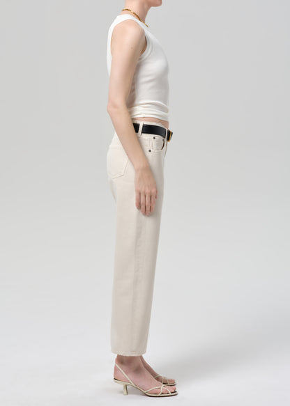 Person wearing a white sleeveless top and beige pants on a light gray background