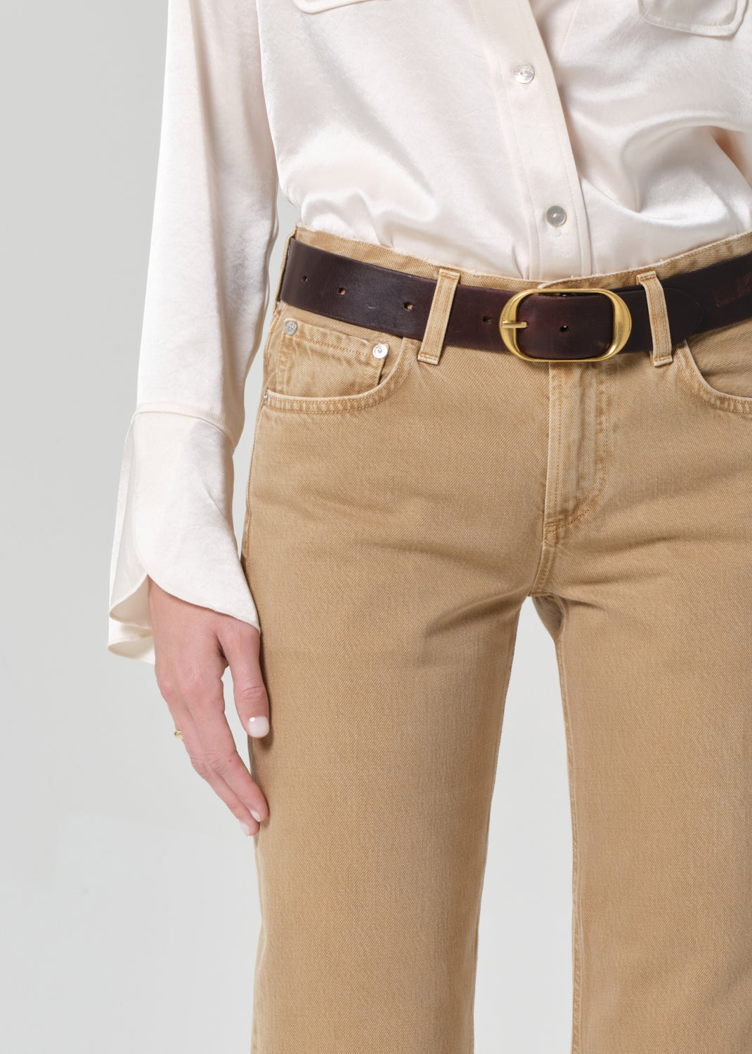 Person wearing beige pants with a brown belt on a plain background