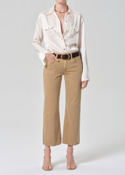 Person wearing a white shirt and beige pants with a belt on a plain background