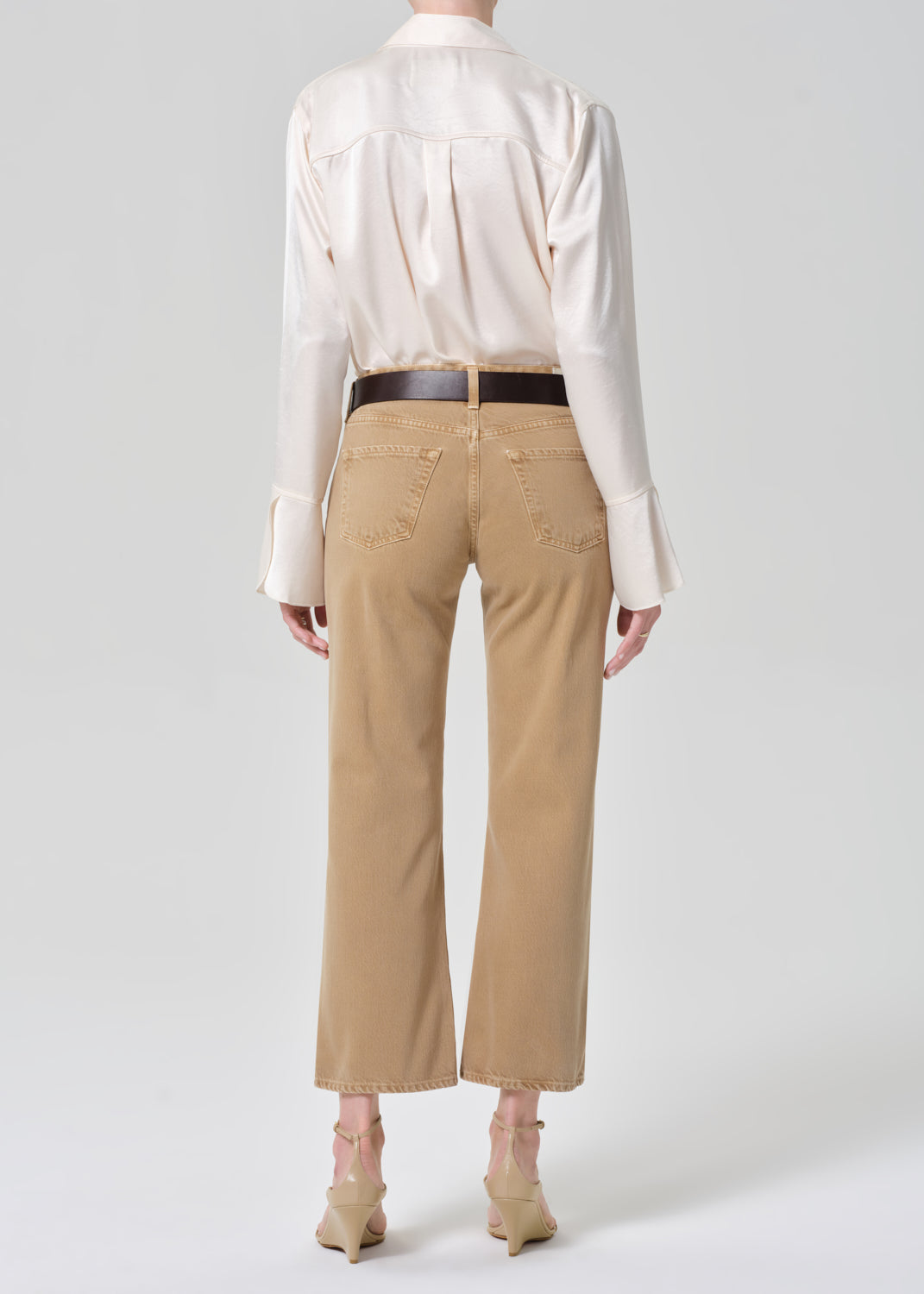 Person wearing a white blouse and beige pants with a black belt on a grey background