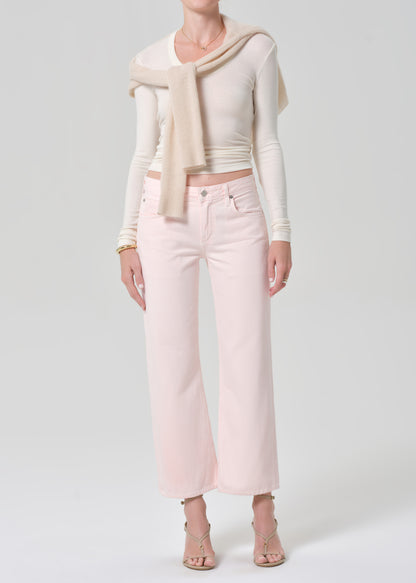 Person wearing a cream top, beige sweater, and light pink jeans on a grey background