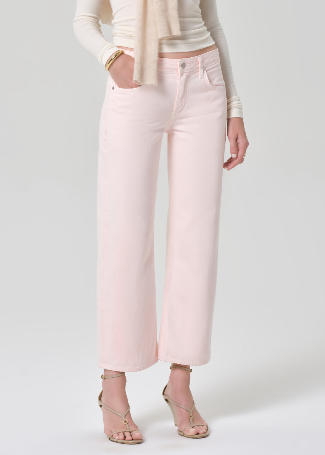 Person wearing a cream top, beige sweater, and light pink jeans on a grey background