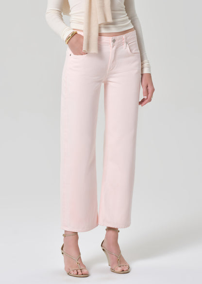 Person wearing a cream top, beige sweater, and light pink jeans on a grey background