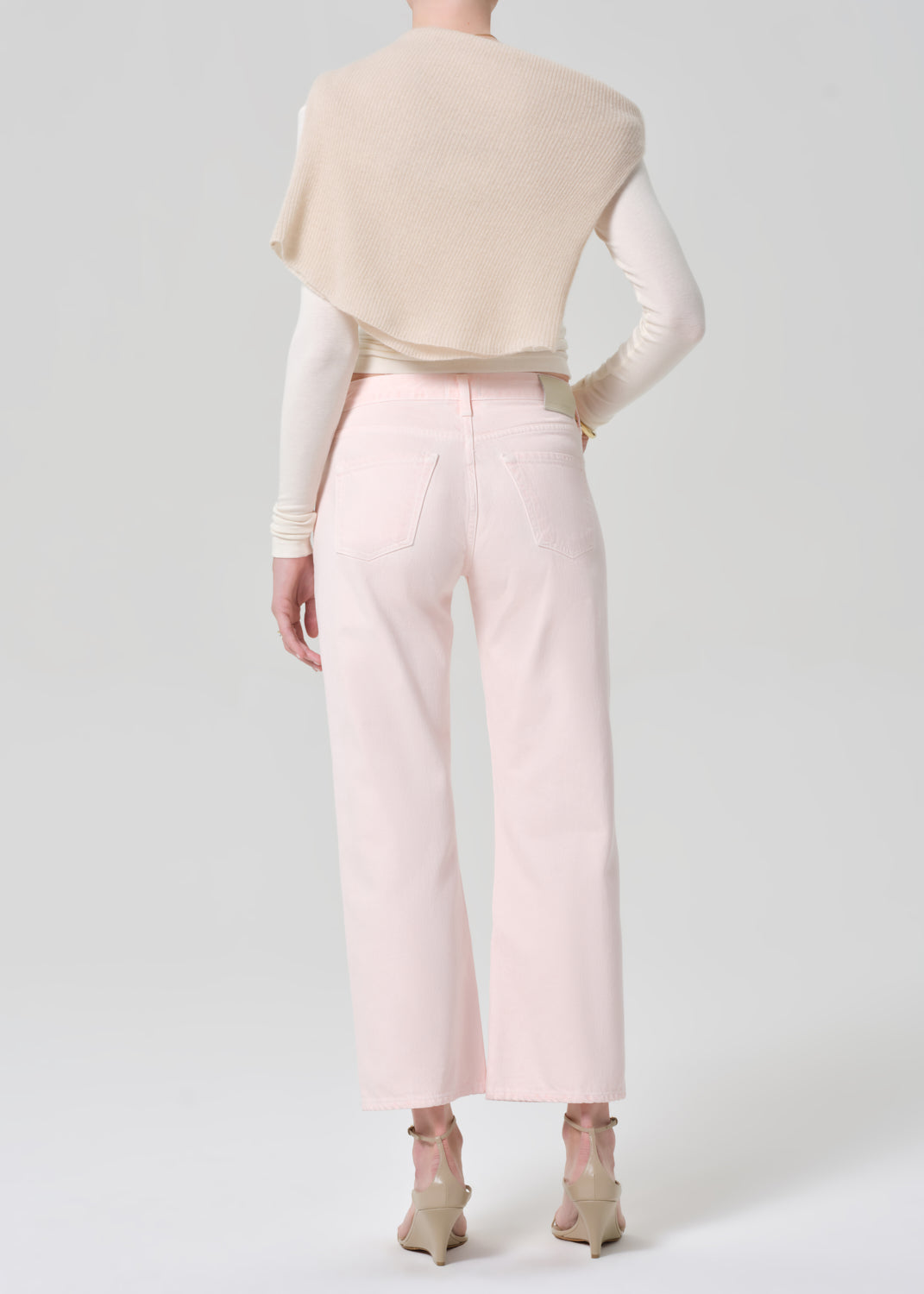 Person wearing a cream top, beige sweater, and light pink jeans on a grey background