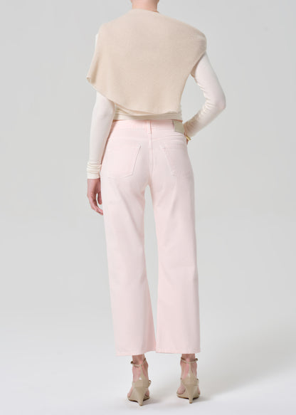 Person wearing a cream top, beige sweater, and light pink jeans on a grey background