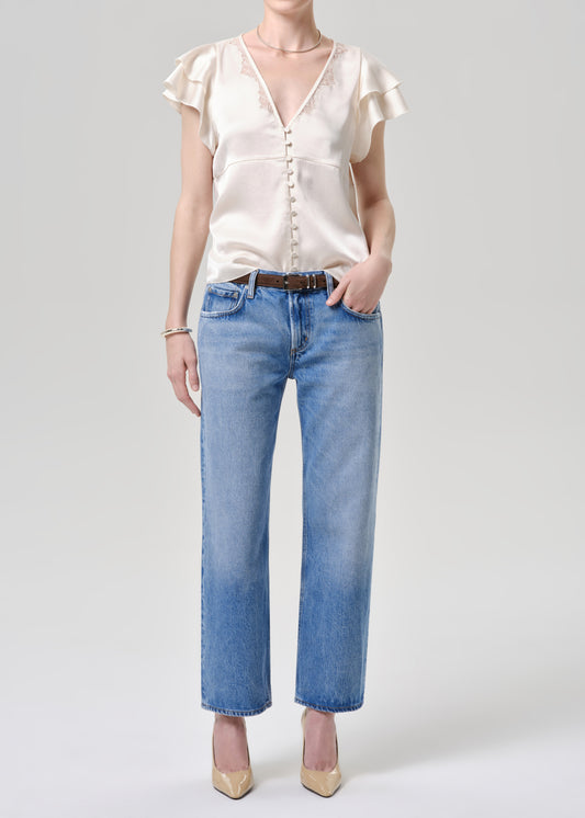 Person wearing a white blouse and blue jeans on a grey background.