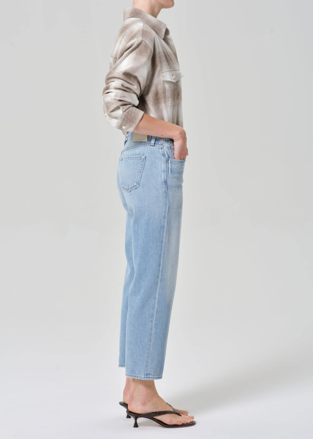 Person wearing a patterned shirt and light blue jeans on a plain background