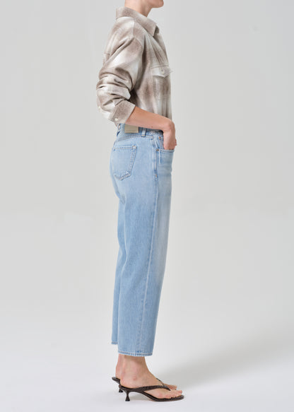 Person wearing a patterned shirt and light blue jeans on a plain background