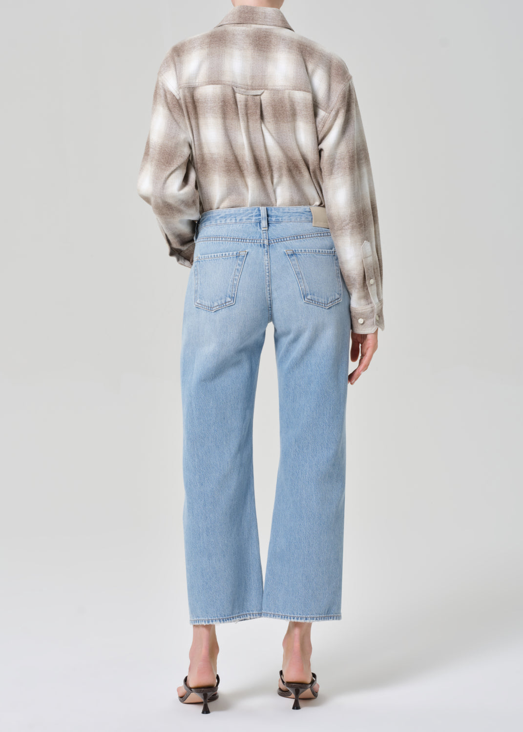 Person wearing a patterned shirt and light blue jeans on a plain background