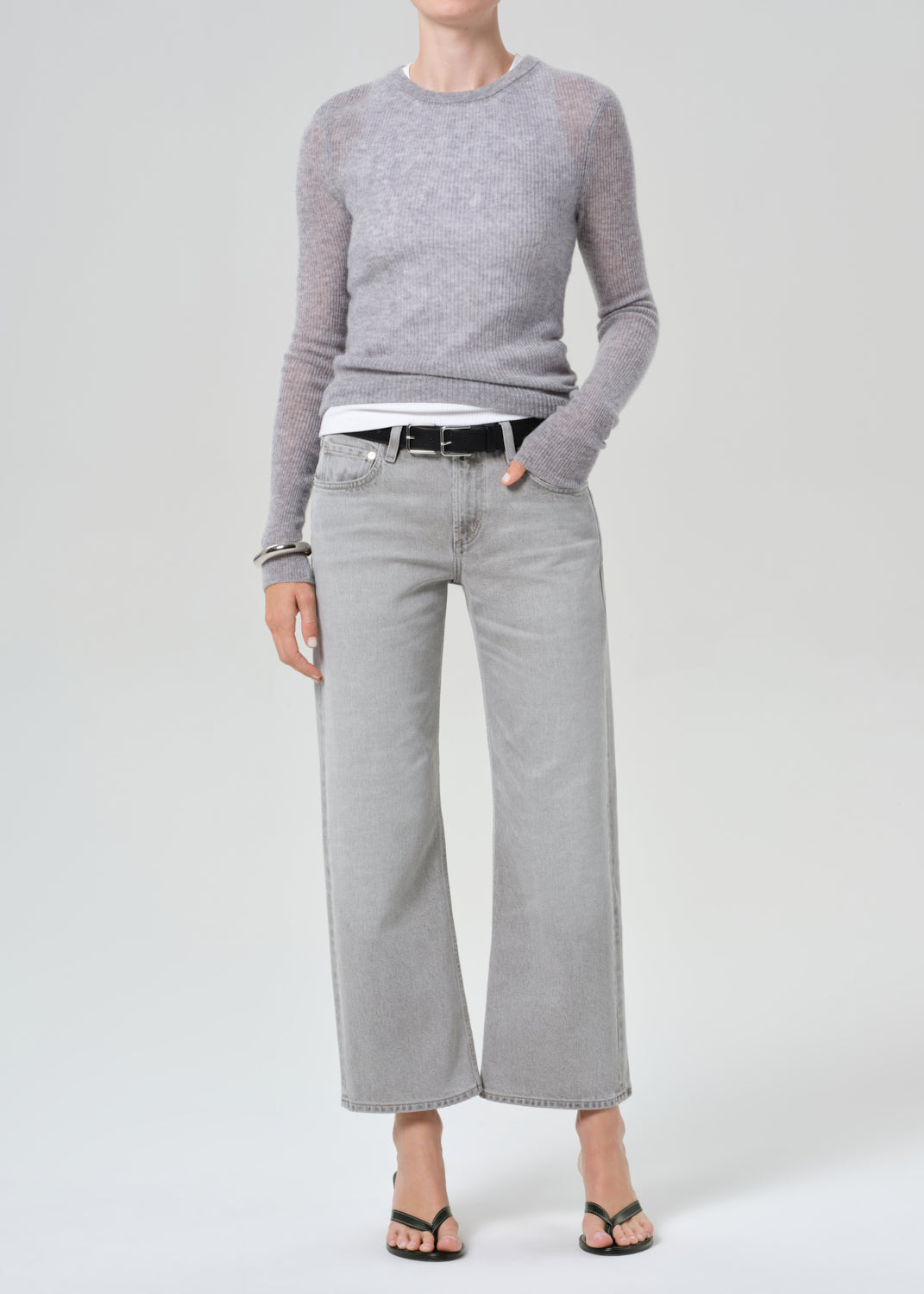 Person wearing a gray sweater and light gray jeans on a white background