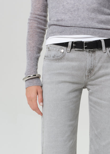 Person wearing a gray sweater, white shirt, black belt, and light gray jeans on a plain background