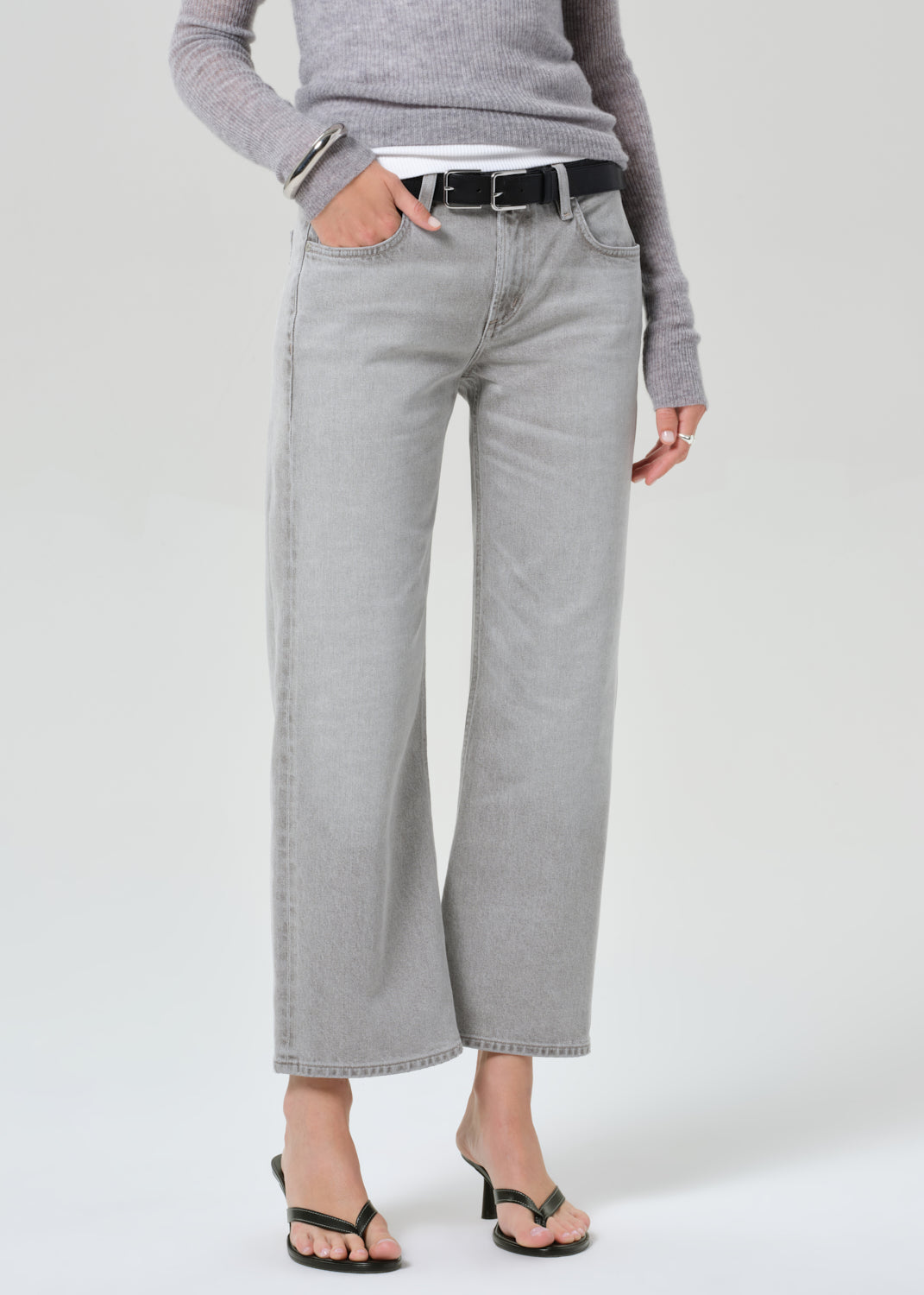 Person wearing gray wide-leg jeans and a gray sweater on a white background