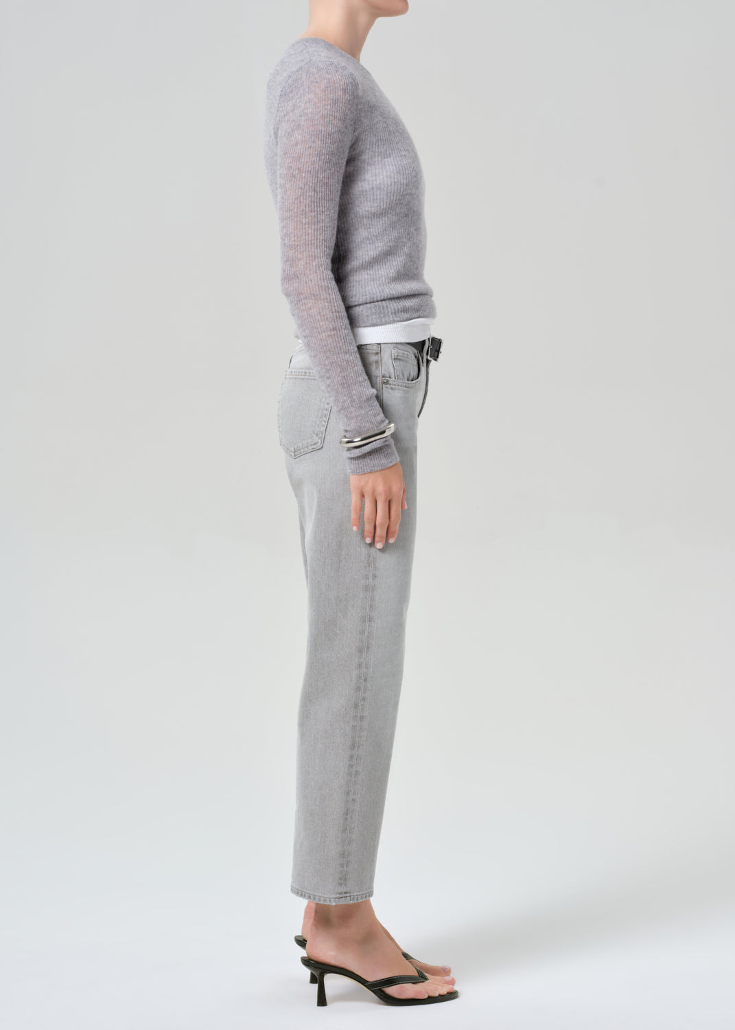 Person wearing a gray sweater and light gray jeans on a white background