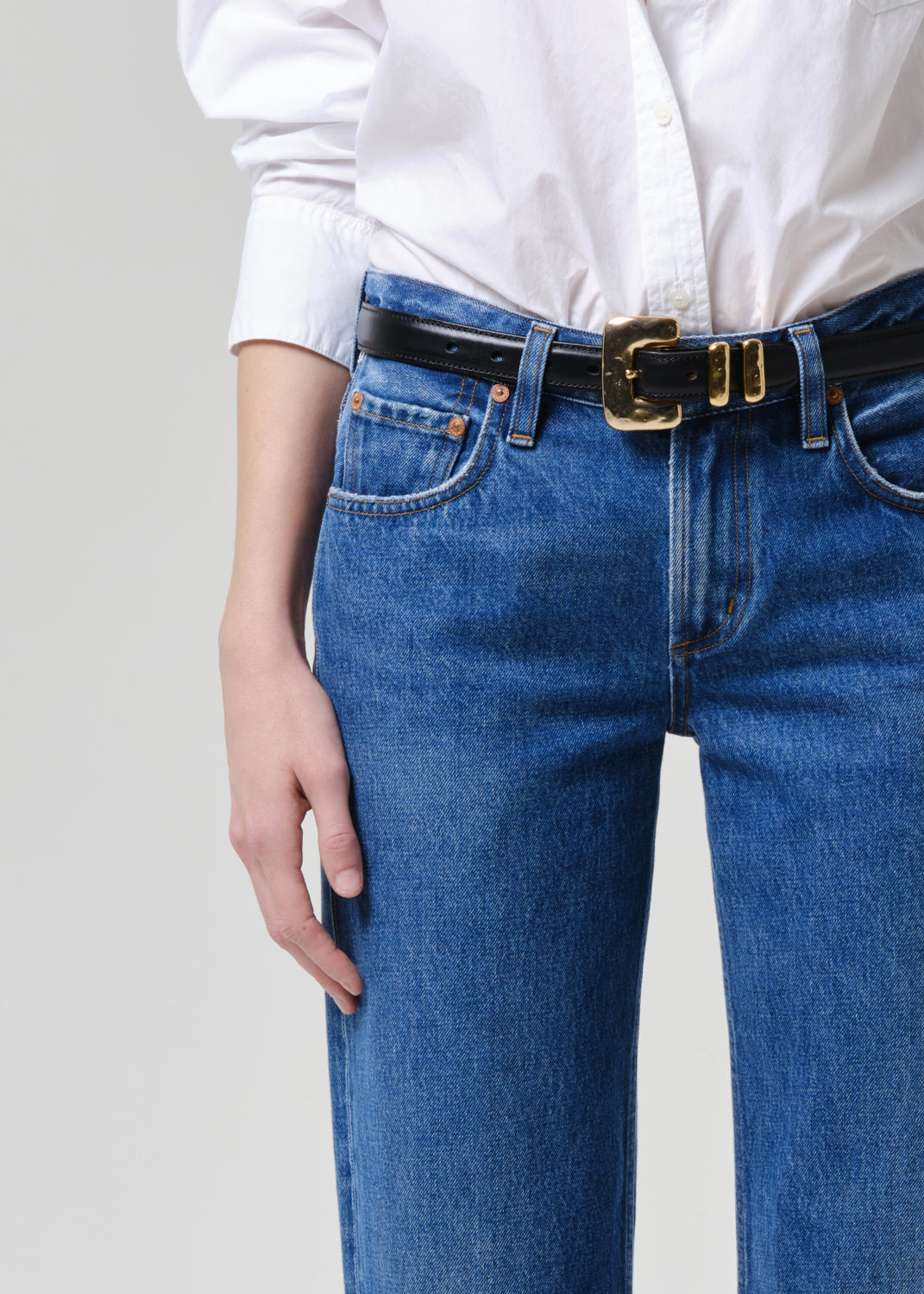 Person wearing blue jeans with a white shirt on a grey background.