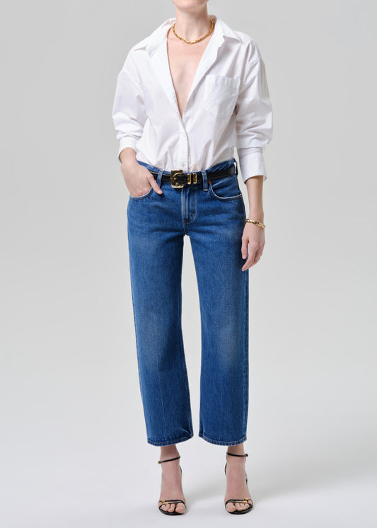 Person wearing a white shirt, blue jeans, and a gold belt on a grey background.
