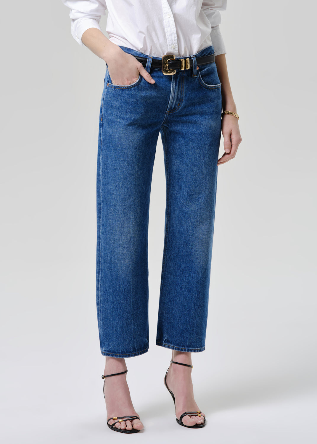 Person wearing blue jeans with a white shirt on a grey background.