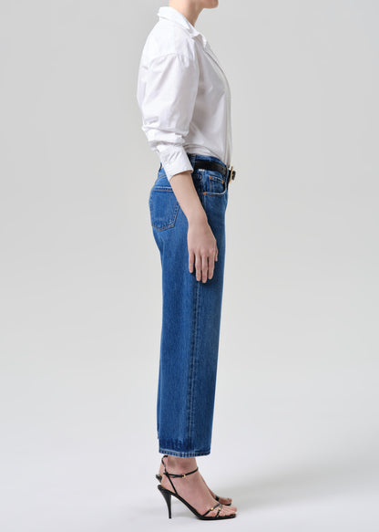 Person wearing a white shirt and blue jeans on a grey background.
