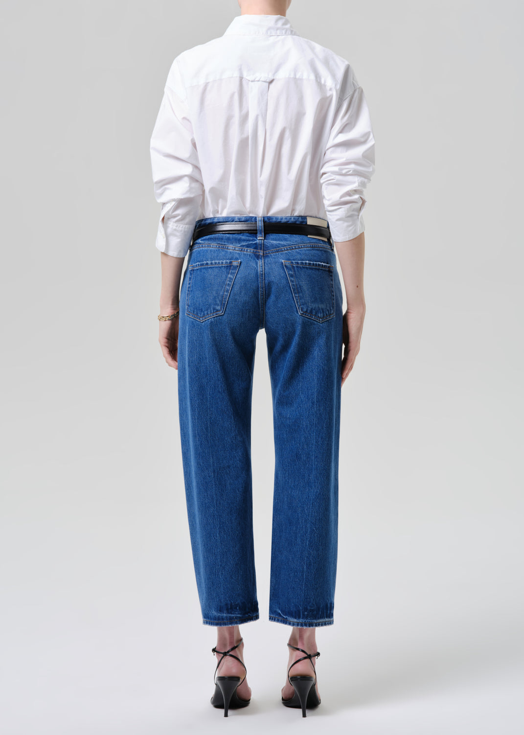 Person wearing a white shirt and blue jeans on a grey background.
