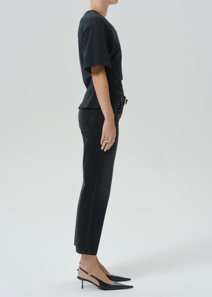 A model shown in profile wearing a black short-sleeve top, black cropped pants, and black slingback heels against a grey background.
