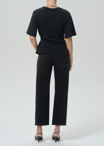 A model shown from the back wearing a black short-sleeve t-shirt and black cropped wide-leg jeans, paired with black pointed-toe heels, against a grey background.