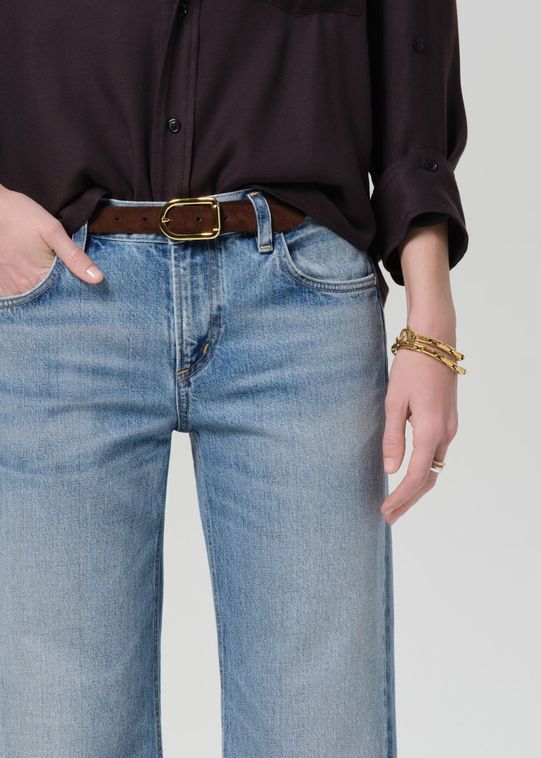 Person wearing a brown shirt and blue jeans on a light gray background