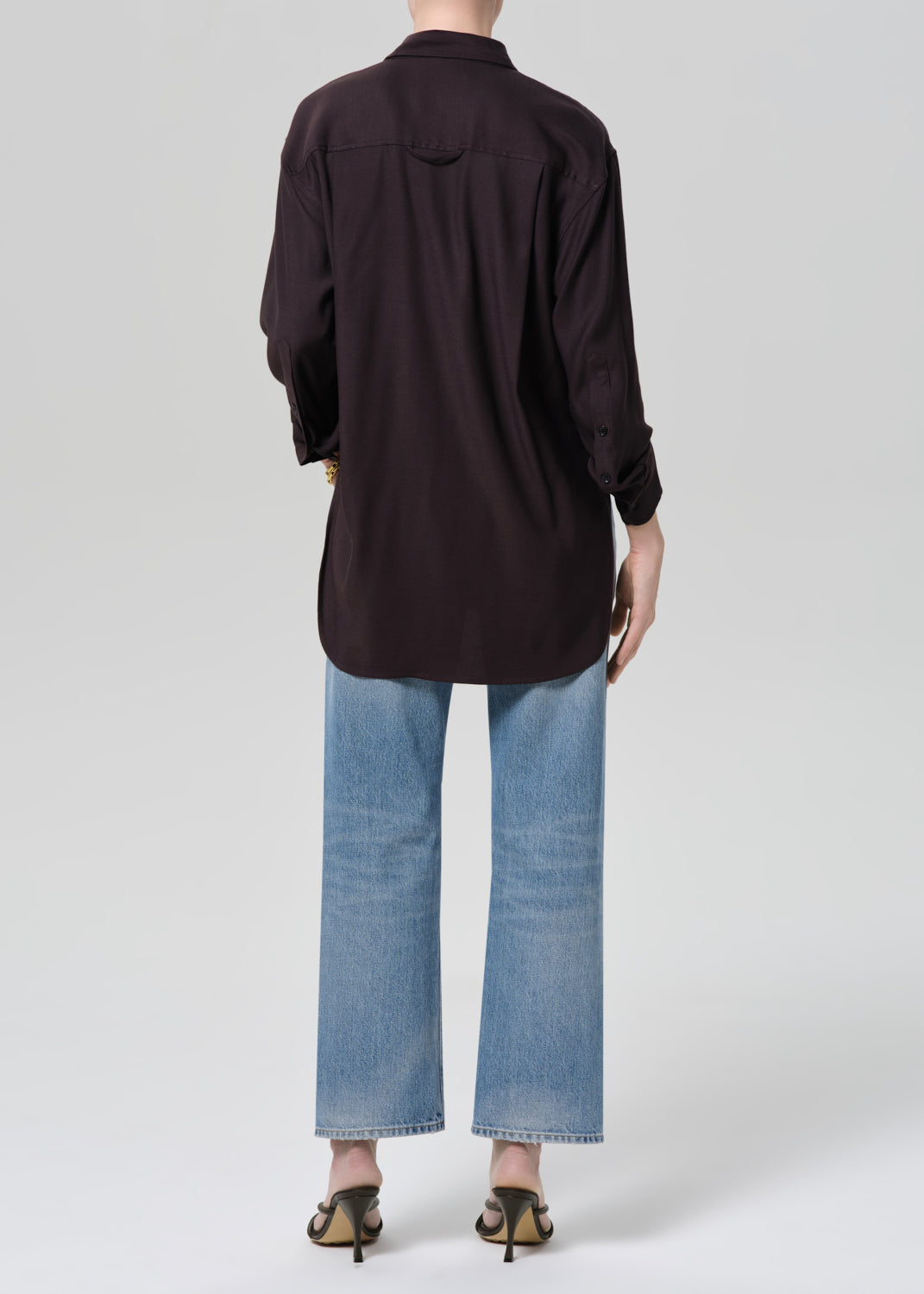 Person wearing a brown shirt and blue jeans on a light gray background