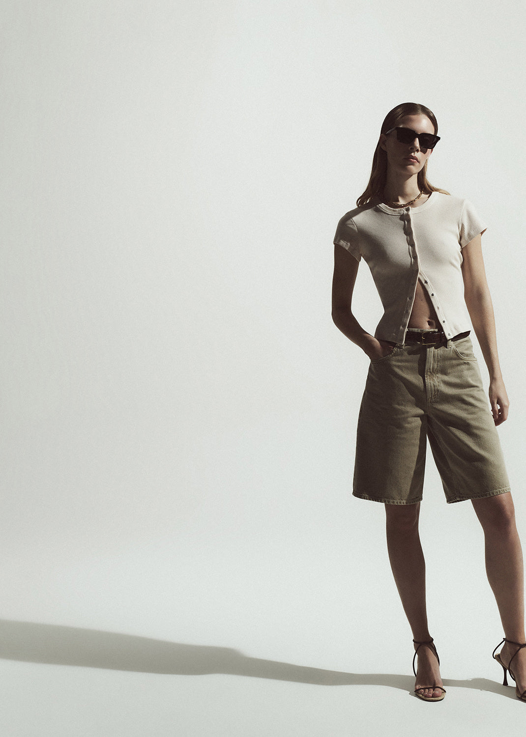 Woman wearing a cardigan and beige shorts on a plain background