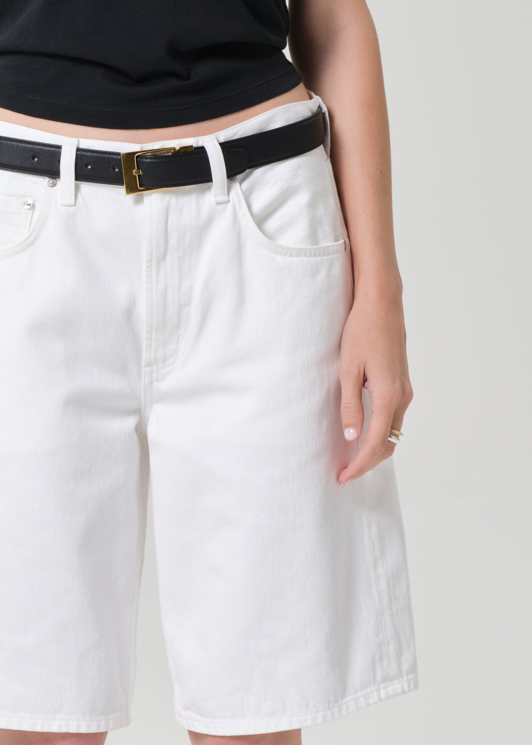 Person wearing a black tee and white denim shorts on a plain background