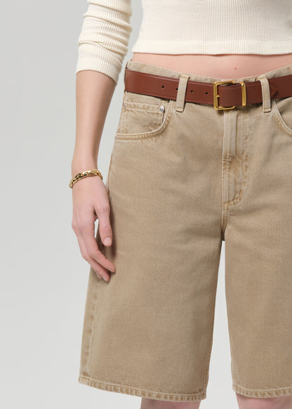 Person wearing beige shorts with a brown belt on a plain background