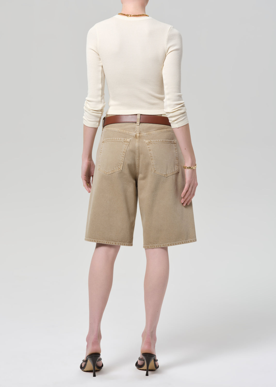 Person wearing a cream top and beige shorts on a grey background