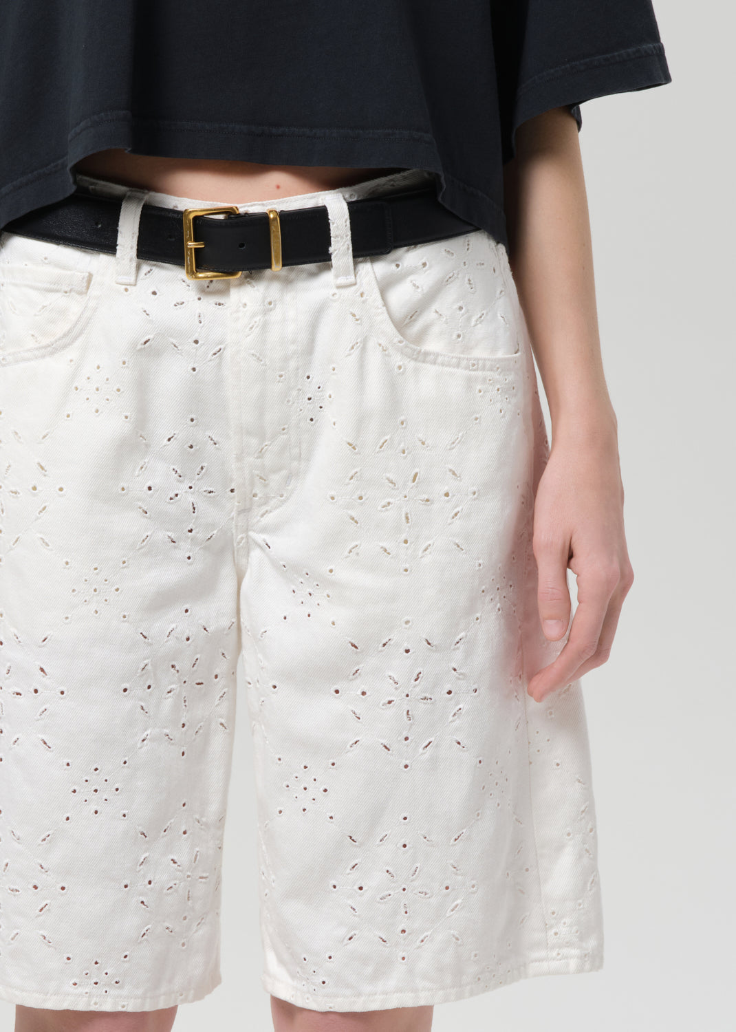 Person wearing white shorts with a subtle pattern and a black belt on a plain background