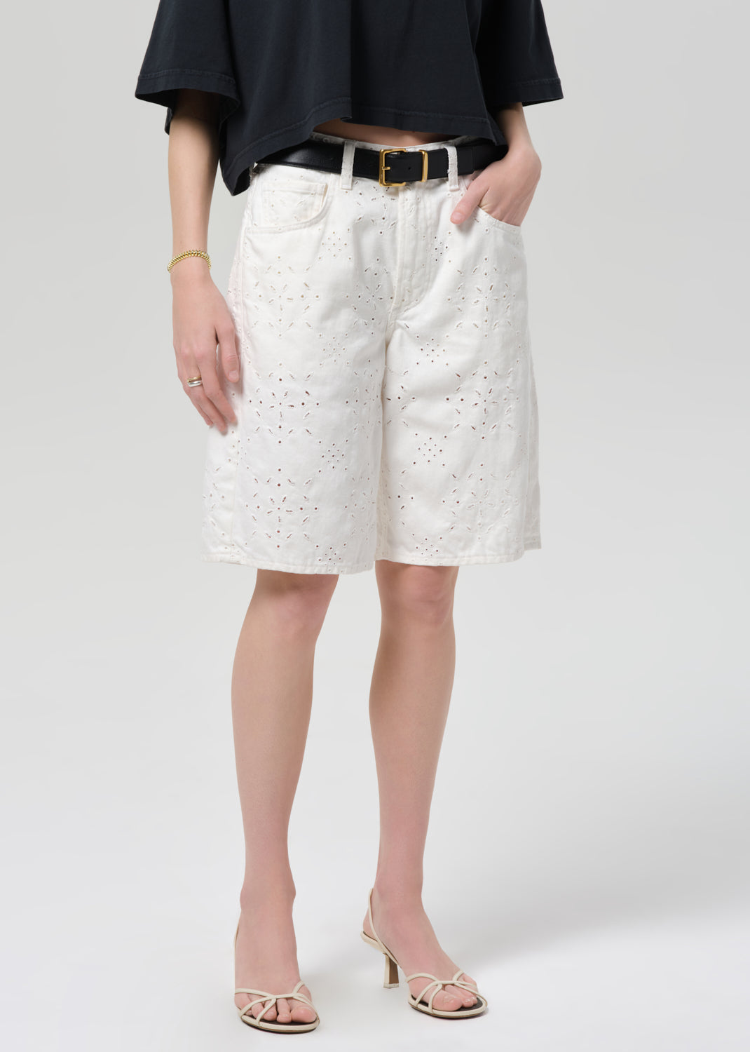 Person wearing a black top and white shorts with a belt on a plain background