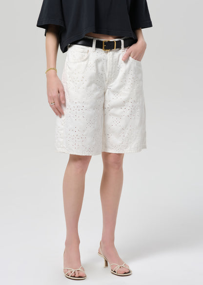 Person wearing a black top and white shorts with a belt on a plain background