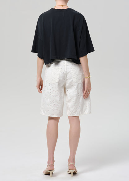 Person wearing a black top and white patterned shorts on a plain background
