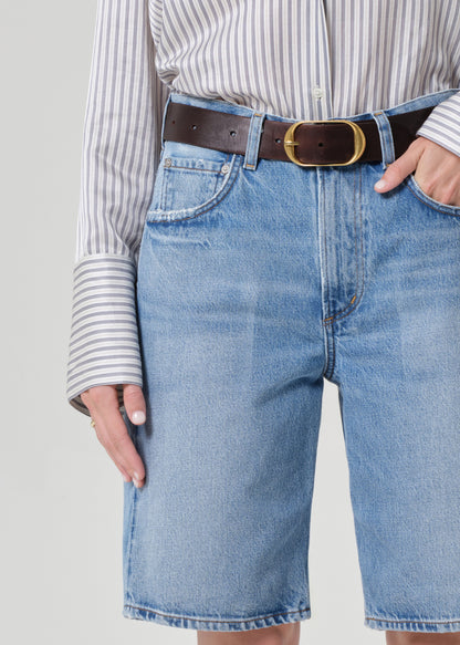 Person wearing a striped shirt and denim shorts on a grey background