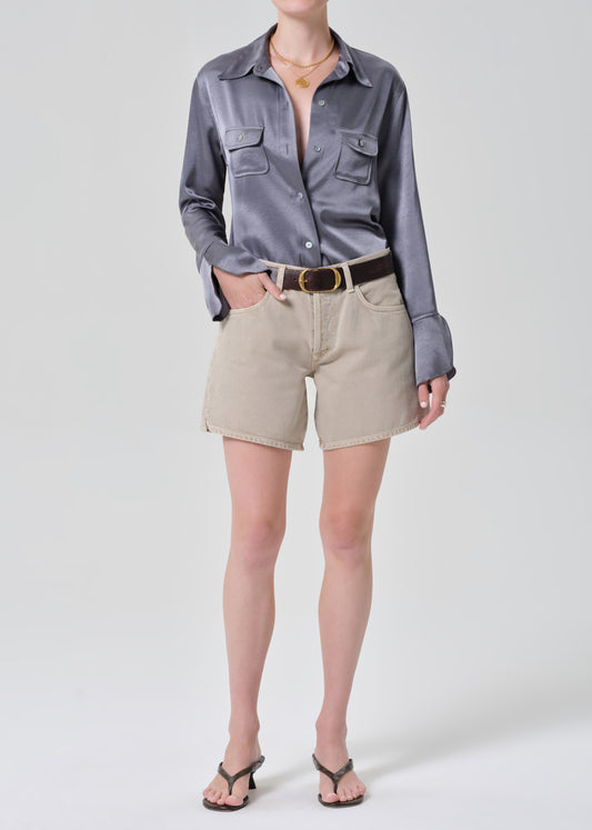 Person wearing a gray button-up shirt and beige shorts on a grey background