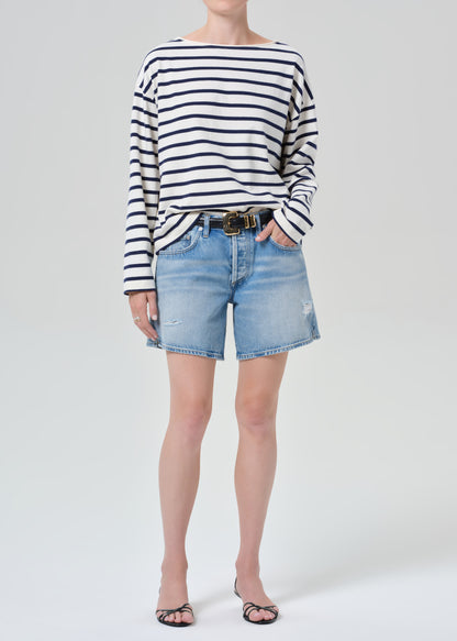 Person wearing a striped shirt and denim shorts on a grey background