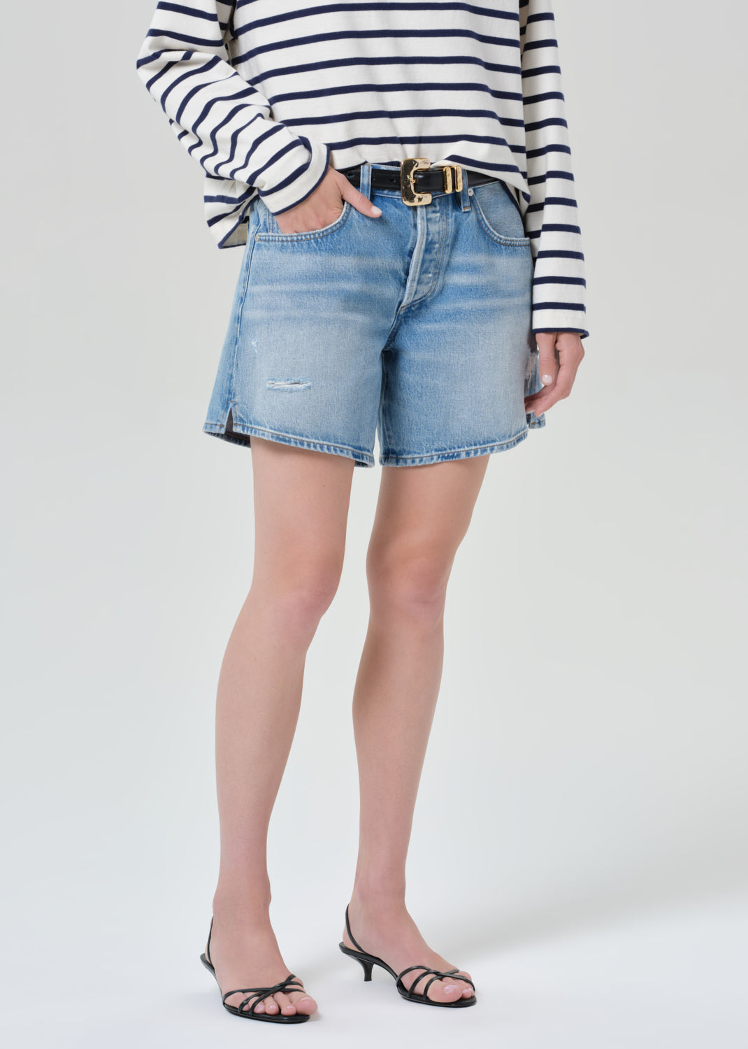 Person wearing a striped shirt and denim shorts on a grey background