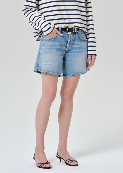 Person wearing a striped shirt and denim shorts on a grey background